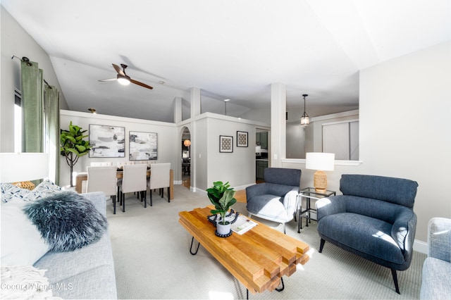 carpeted living area with arched walkways, baseboards, ceiling fan, and vaulted ceiling