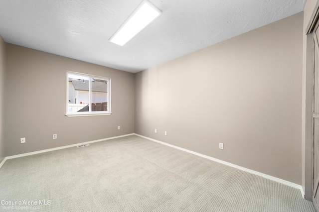 empty room featuring light colored carpet, baseboards, and a textured ceiling