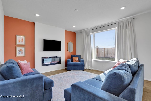 living area featuring a glass covered fireplace, recessed lighting, wood finished floors, and baseboards