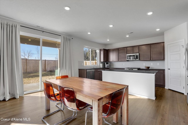 kitchen featuring wood finished floors, recessed lighting, dark brown cabinets, appliances with stainless steel finishes, and a center island