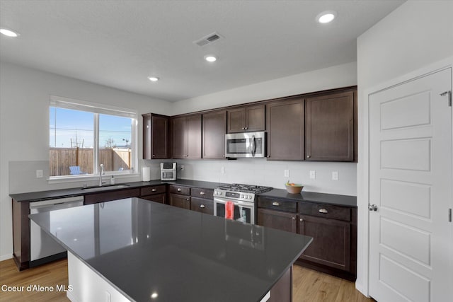 kitchen featuring light wood finished floors, a sink, dark brown cabinetry, appliances with stainless steel finishes, and dark countertops