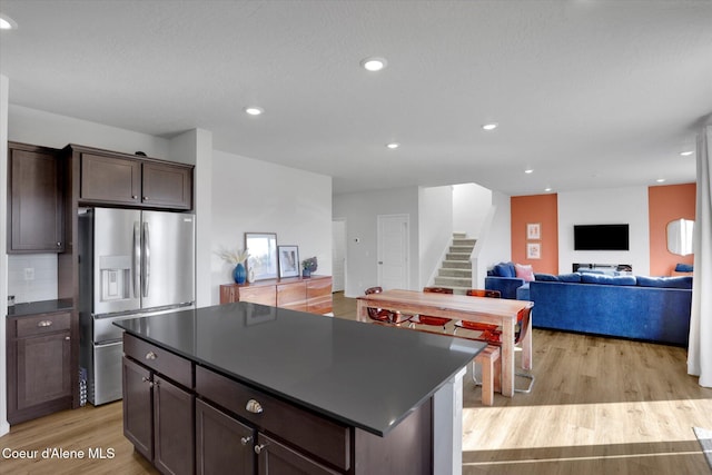 kitchen with dark brown cabinetry, light wood-style floors, stainless steel refrigerator with ice dispenser, dark countertops, and a center island