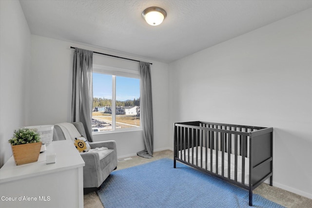 bedroom with a crib, baseboards, carpet floors, and a textured ceiling