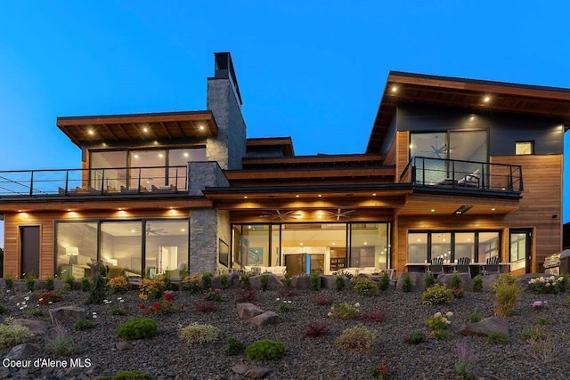 rear view of house with a balcony, ceiling fan, and a chimney