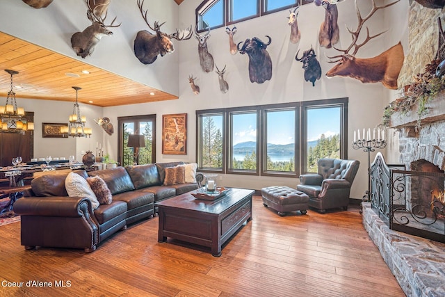 living room with wood-type flooring, a high ceiling, a stone fireplace, and wooden ceiling