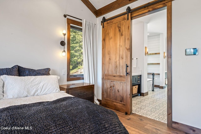 bedroom with wood finished floors, baseboards, ensuite bath, vaulted ceiling with beams, and a barn door