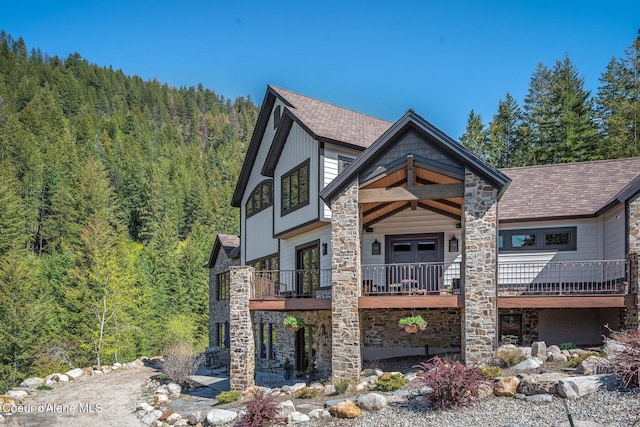 view of front of home with a wooded view, stone siding, and a shingled roof