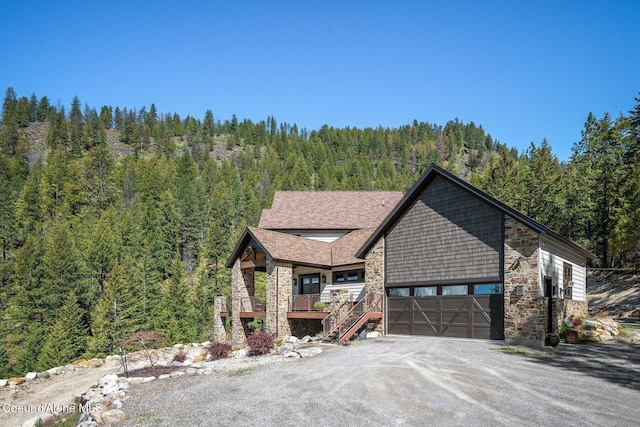 view of front of house featuring stairs, driveway, a forest view, and stone siding