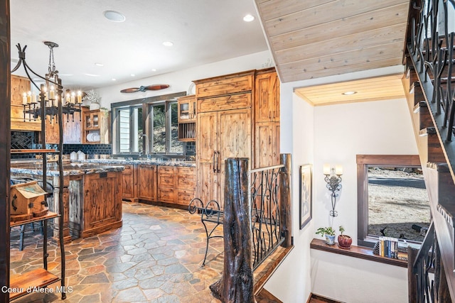 kitchen featuring tasteful backsplash, stone tile flooring, recessed lighting, brown cabinetry, and glass insert cabinets