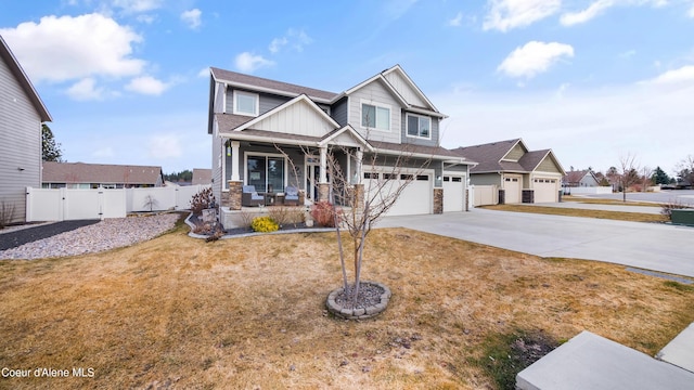 craftsman inspired home with fence, an attached garage, covered porch, concrete driveway, and stone siding