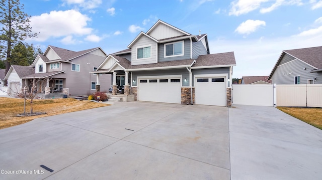 craftsman-style home with a gate, stone siding, fence, board and batten siding, and concrete driveway