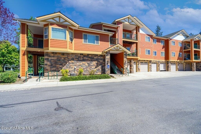 multi unit property featuring stone siding, stairway, and a garage