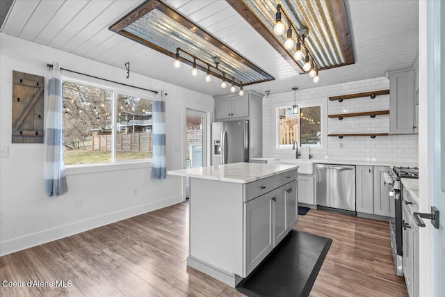 kitchen with gray cabinetry, wood finished floors, stainless steel appliances, light countertops, and decorative backsplash