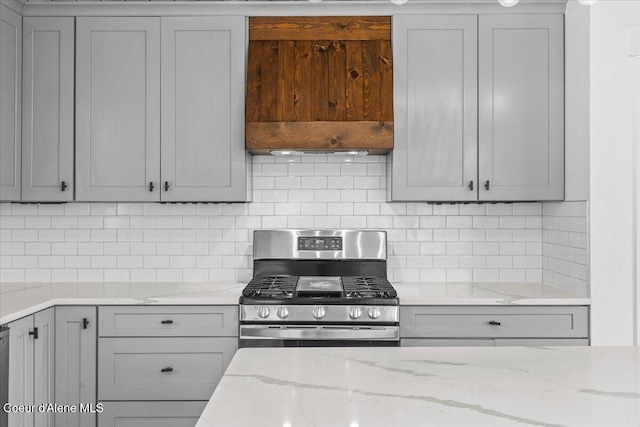 kitchen featuring light stone countertops, gray cabinets, backsplash, and stainless steel gas range oven