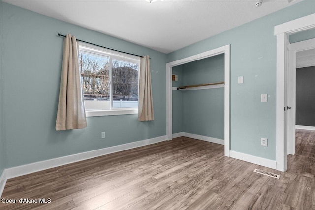 unfurnished bedroom with a closet, visible vents, baseboards, and wood finished floors