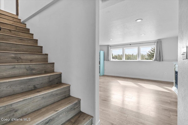 staircase with recessed lighting, a textured ceiling, baseboards, and wood finished floors