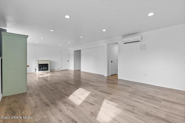 unfurnished living room featuring a wall unit AC, recessed lighting, a fireplace, and light wood-style floors