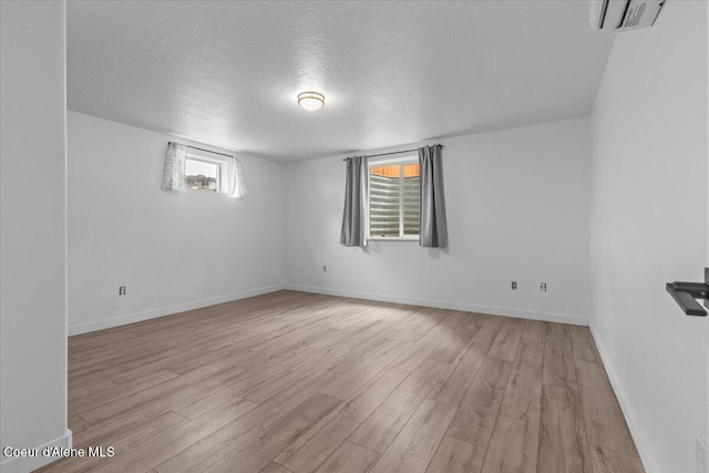 empty room with light wood-style flooring, an AC wall unit, a textured ceiling, and baseboards