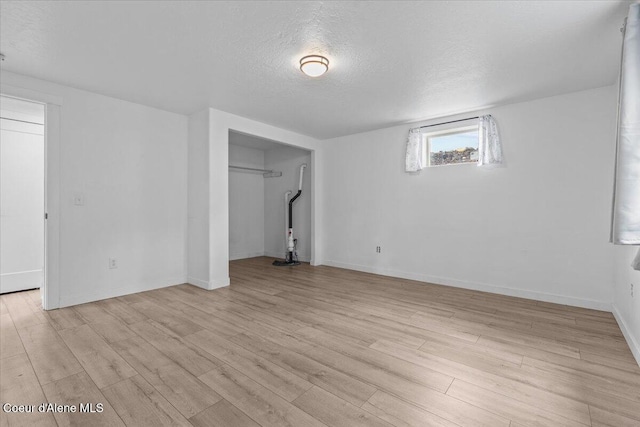 basement with baseboards, a textured ceiling, and light wood-style floors