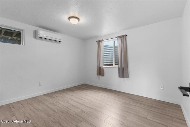 unfurnished room with baseboards, a textured ceiling, an AC wall unit, and wood finished floors