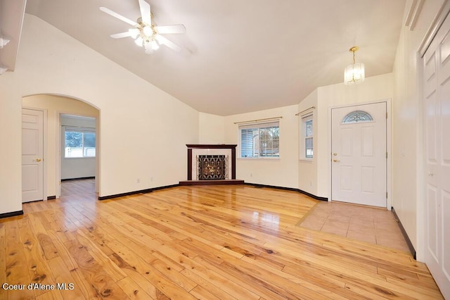 foyer entrance featuring light wood finished floors, arched walkways, baseboards, and vaulted ceiling