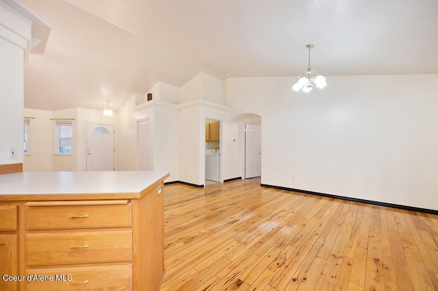 kitchen featuring light wood finished floors, washer / dryer, arched walkways, and vaulted ceiling