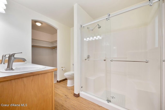 bathroom with a walk in closet, toilet, a sink, wood finished floors, and a shower stall