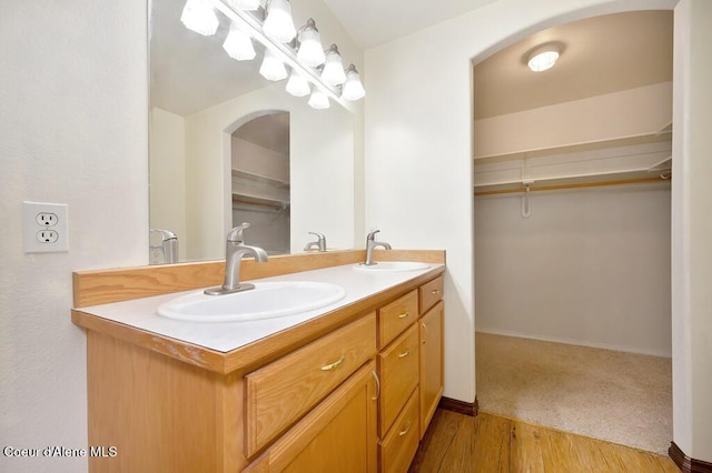 bathroom featuring a sink, a walk in closet, wood finished floors, and double vanity