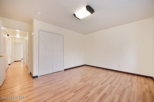 unfurnished bedroom featuring a closet, light wood-type flooring, and baseboards