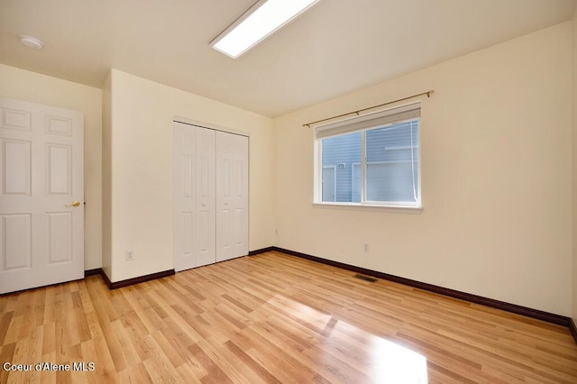 unfurnished bedroom with a closet, visible vents, baseboards, and light wood finished floors