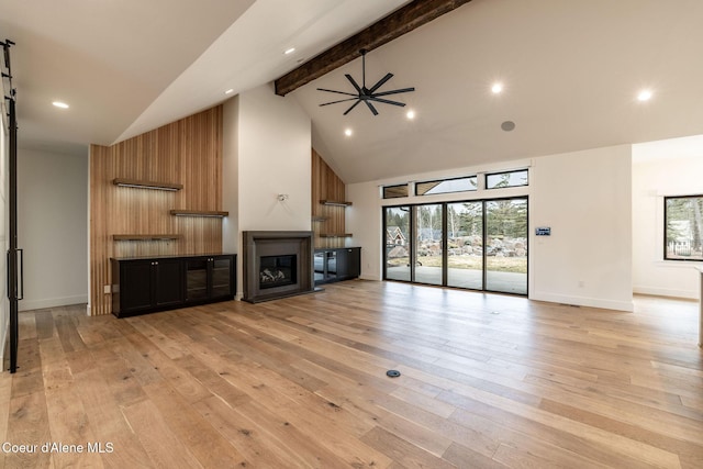 unfurnished living room featuring baseboards, beamed ceiling, light wood-style floors, a glass covered fireplace, and high vaulted ceiling