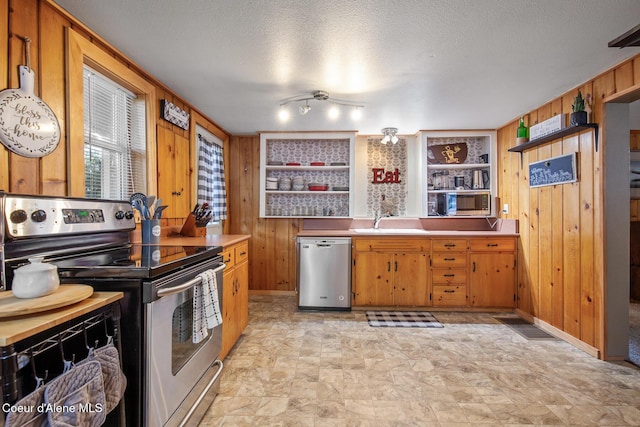 kitchen with wooden walls, open shelves, a sink, stainless steel appliances, and a textured ceiling