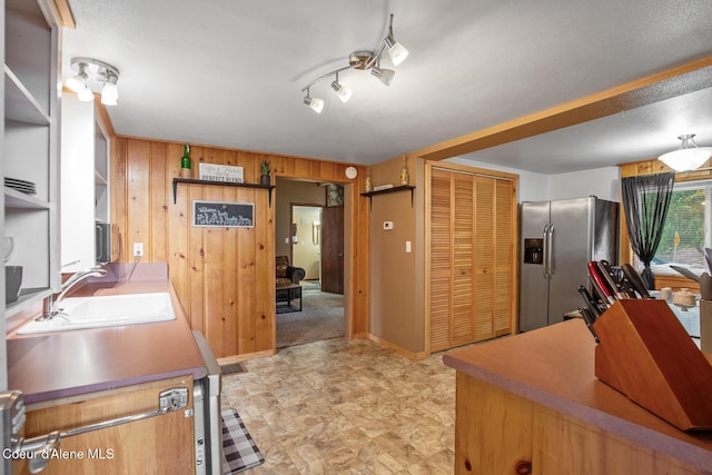 kitchen featuring baseboards, open shelves, stainless steel fridge with ice dispenser, a sink, and wood walls