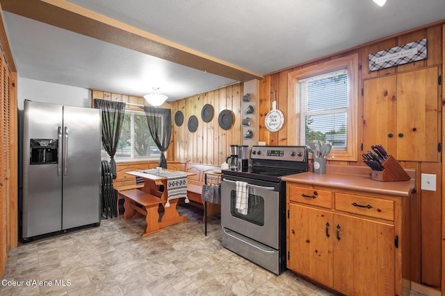 kitchen with light countertops, brown cabinetry, wood walls, and stainless steel appliances