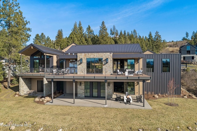 back of house featuring a lawn, metal roof, a patio area, stone siding, and a standing seam roof