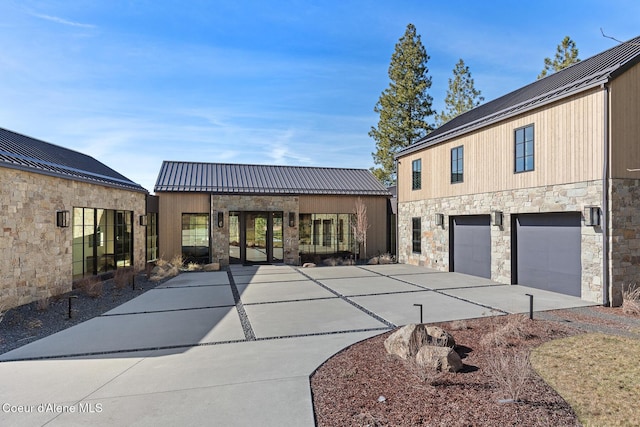 exterior space with a standing seam roof, stone siding, concrete driveway, an attached garage, and metal roof