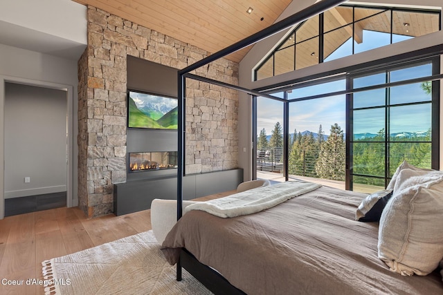 bedroom with high vaulted ceiling, access to outside, wood finished floors, a stone fireplace, and wood ceiling