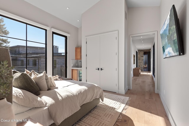 bedroom with a closet, baseboards, high vaulted ceiling, and light wood finished floors