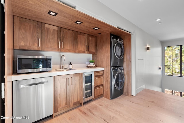 kitchen featuring stacked washing maching and dryer, light wood-style flooring, a sink, stainless steel appliances, and wine cooler