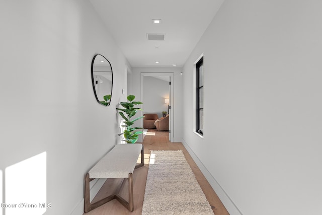 hallway featuring baseboards, visible vents, and light wood finished floors