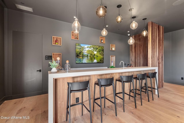 bar featuring hanging light fixtures, light wood-style floors, and baseboards