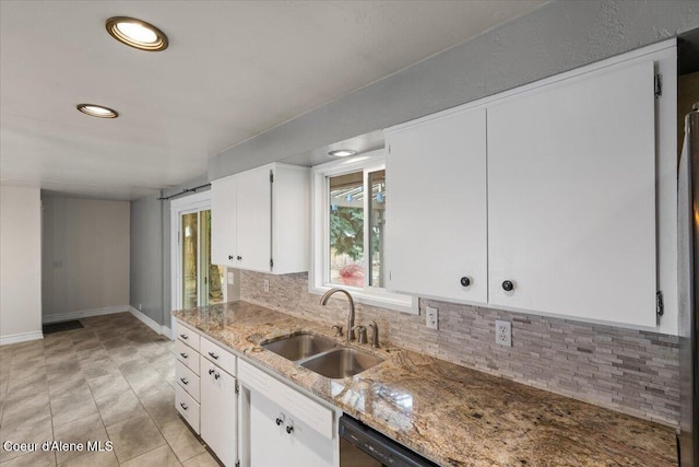 kitchen featuring tasteful backsplash, baseboards, light stone countertops, white cabinetry, and a sink