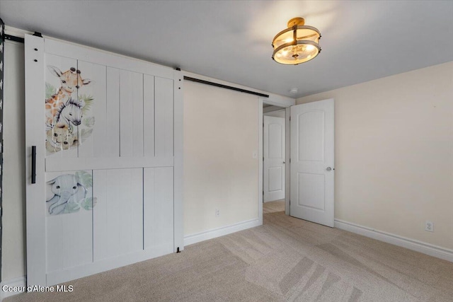 unfurnished bedroom with baseboards, a barn door, and carpet floors