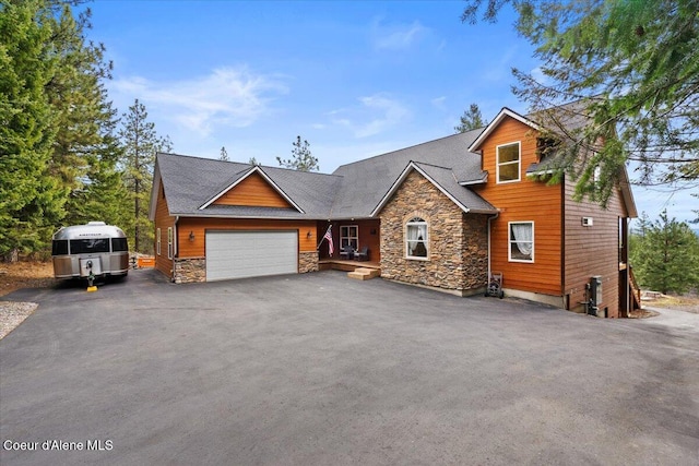 rustic home featuring aphalt driveway, stone siding, and an attached garage