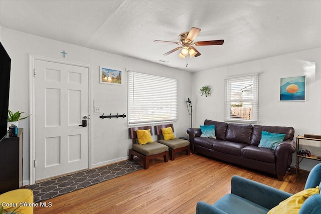 living area with a textured ceiling, wood finished floors, baseboards, and ceiling fan