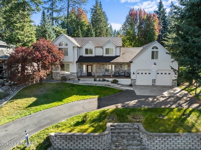 view of front facade with stone siding, board and batten siding, covered porch, concrete driveway, and a front yard