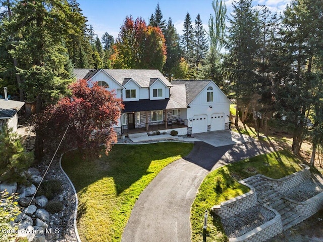 view of front of house with a porch, driveway, an attached garage, and a front lawn