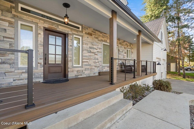 entrance to property featuring stone siding, roof with shingles, and covered porch