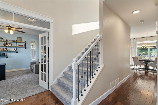 staircase featuring visible vents, baseboards, wood finished floors, and ceiling fan with notable chandelier