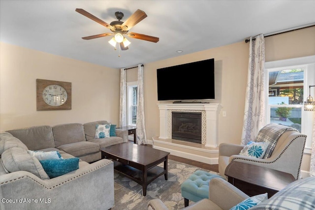 living area with a high end fireplace, a ceiling fan, and wood finished floors